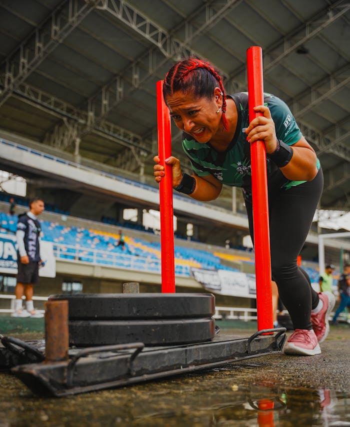 Focused woman athlete pushing a heavy sled during a competition at an outdoor stadium.